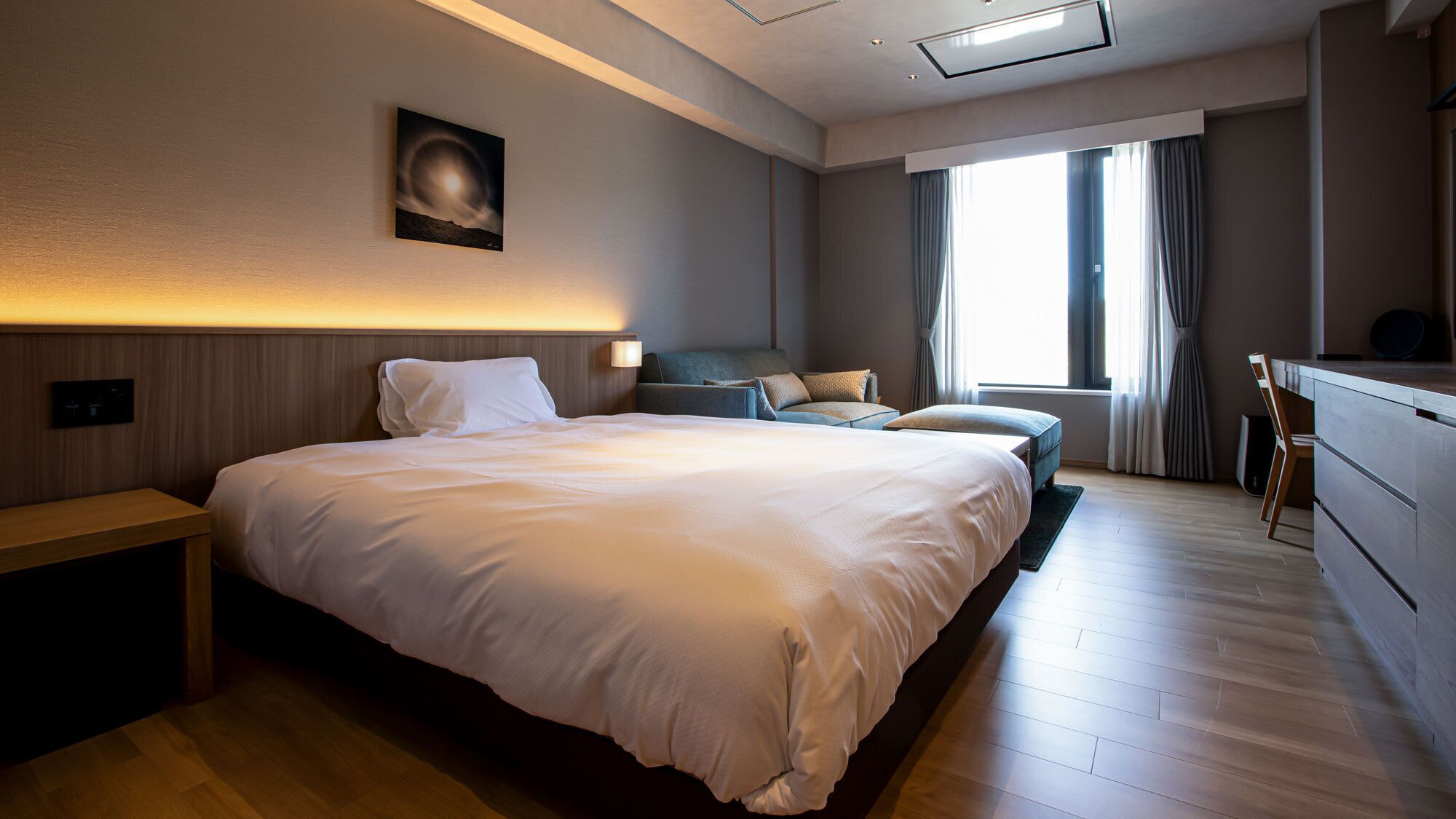 A modern hotel room with a large bed, a desk, and a view of the city.