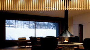 Un salon chaleureux avec une cheminée, de grandes fenêtres donnant sur un paysage enneigé et un design moderne au niveau du plafond.