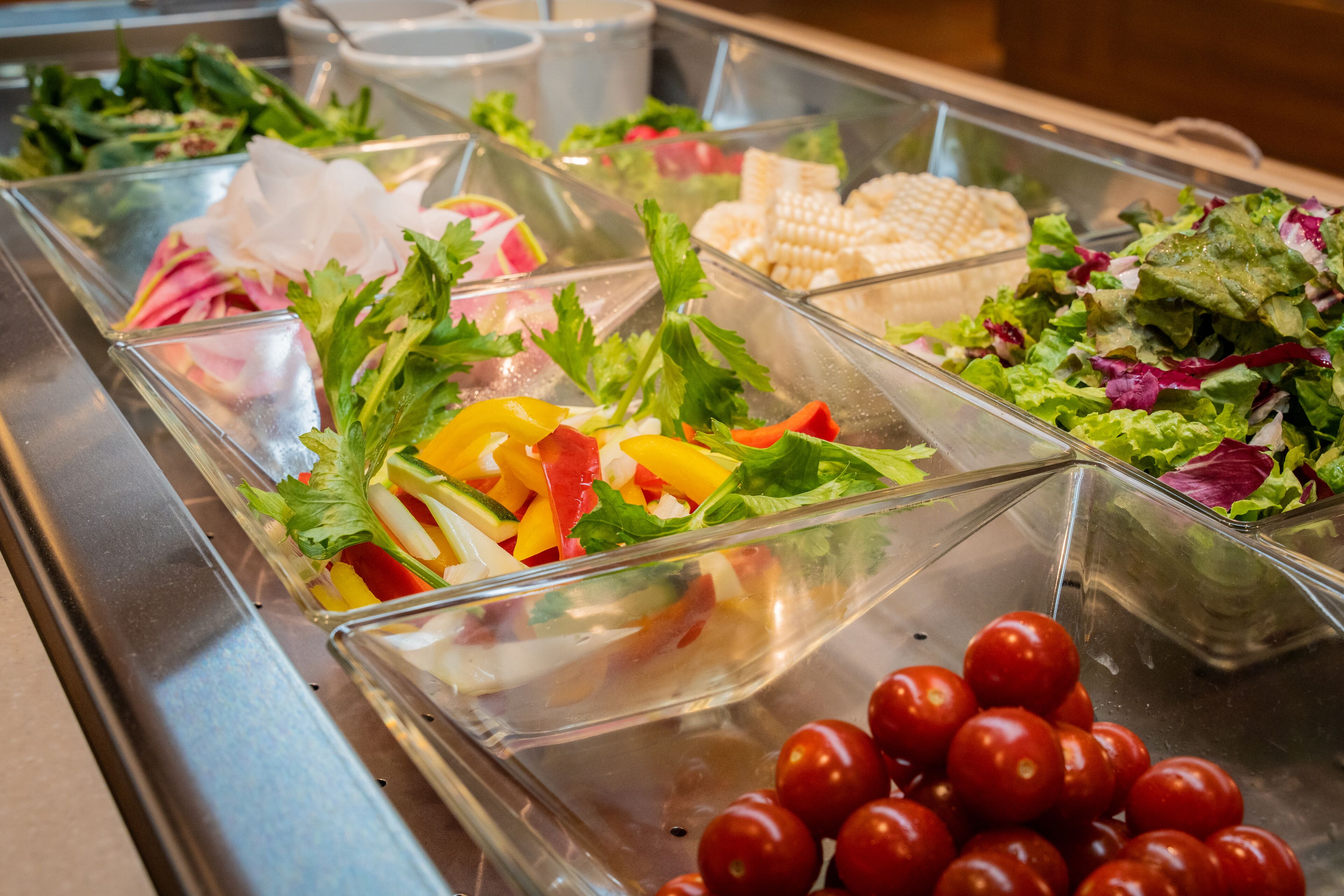 A buffet with various salads and fresh vegetables.