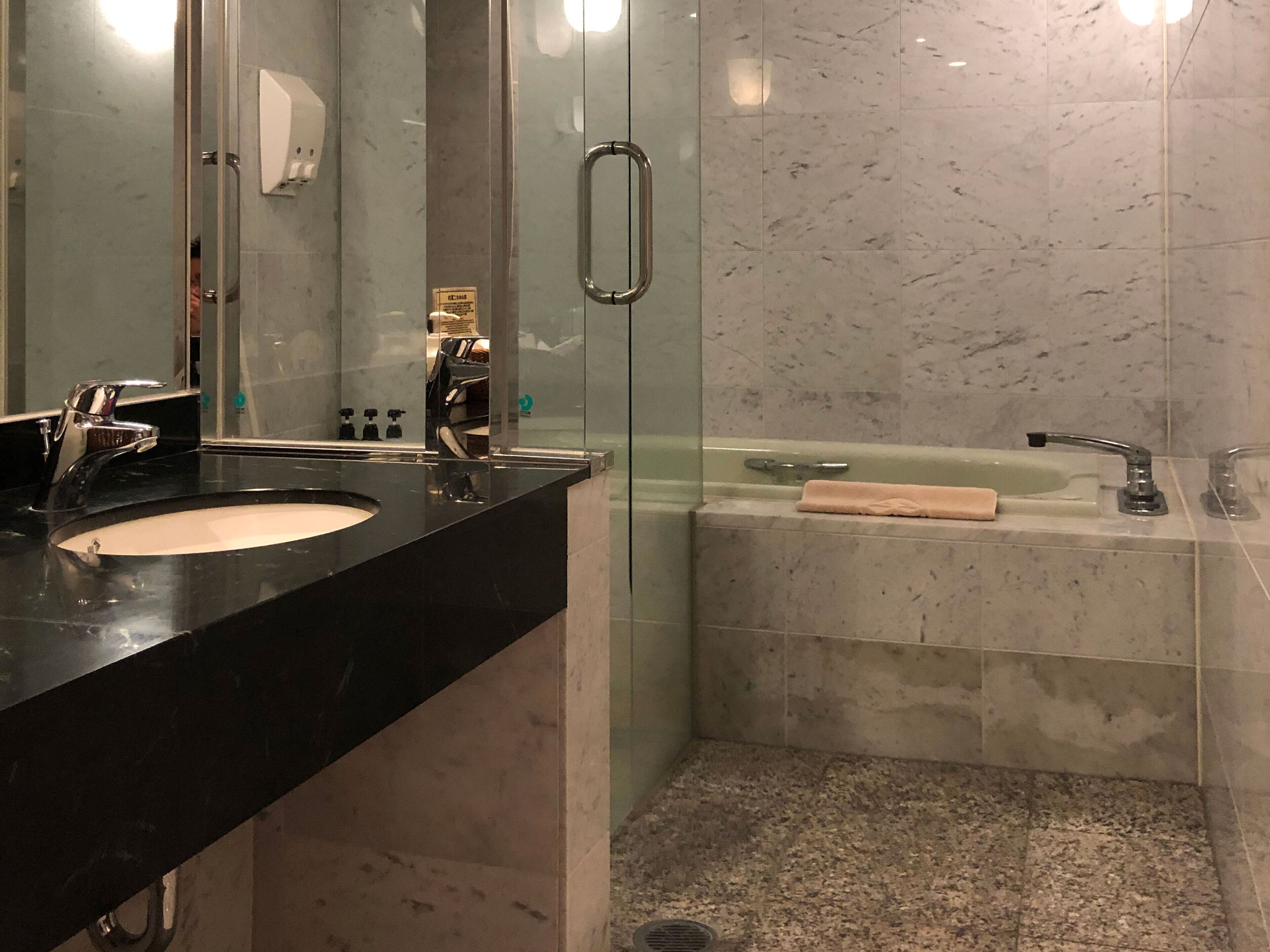 Un bany modern amb un lavabo de taulell negre, dutxa amb envàs de vidre i paret revestida de marbre.