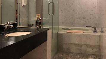 Un bany modern amb un lavabo de taulell negre, dutxa amb envàs de vidre i paret revestida de marbre.