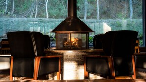 Une cheminée avec un foyer en verre, deux fauteuils en cuir et un manteau de cheminée en pierre.