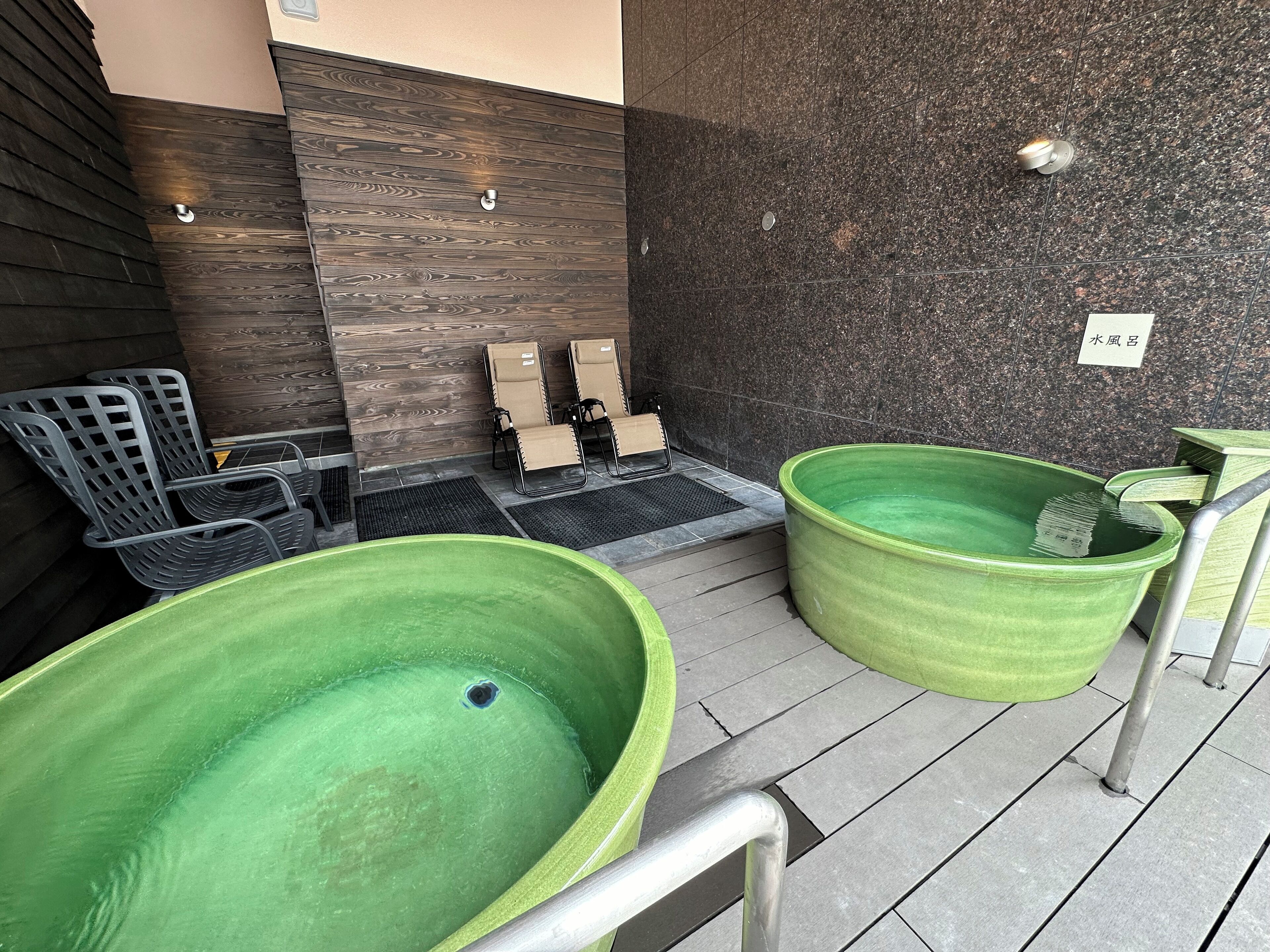 A spa area with two large green tubs, a seating area with chairs, and a wall with a wooden panel design.