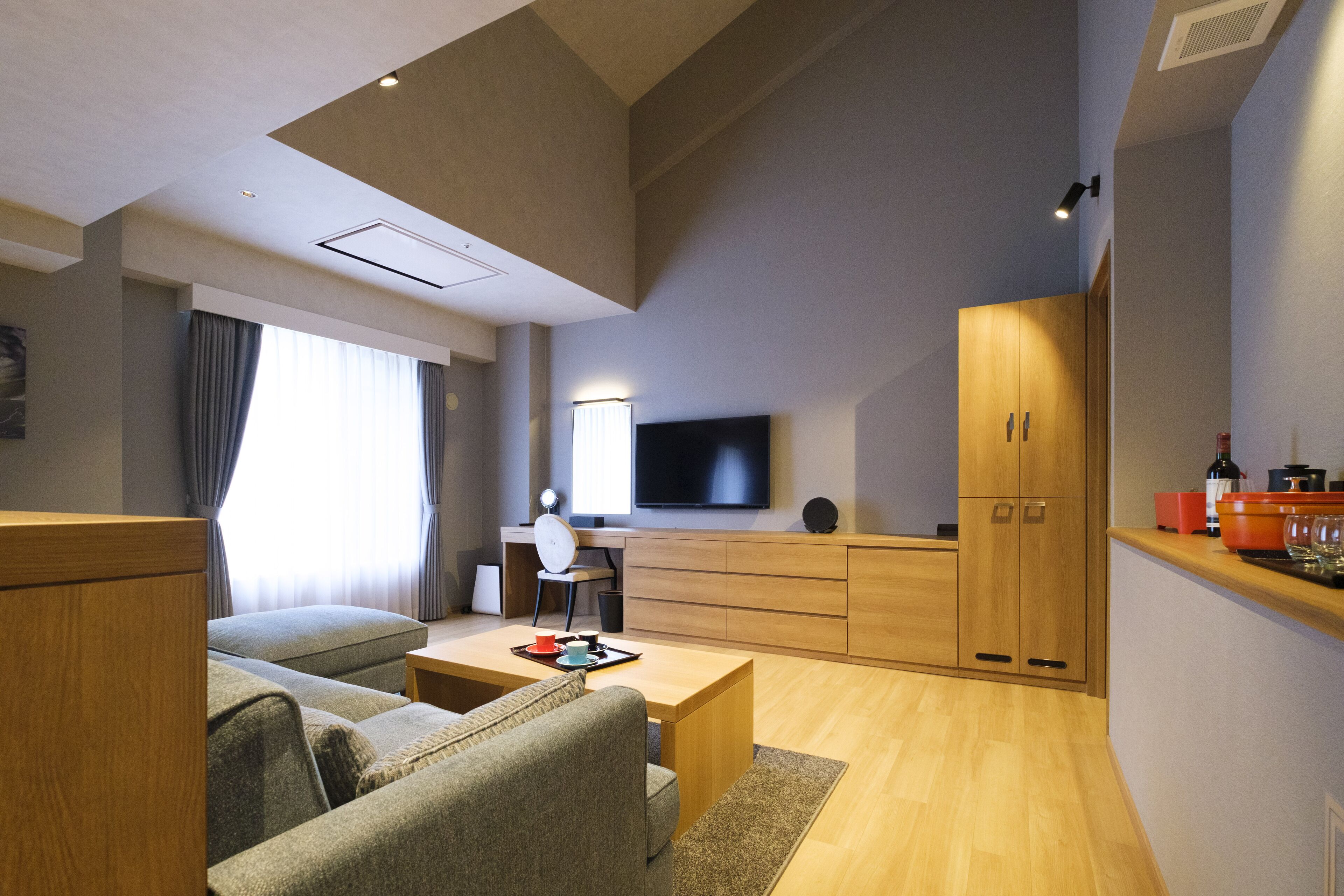 Una sala moderna con un sofá, una mesa de centro y un televisor. Hay una zona de cocina con armarios de madera y una encimera.