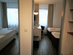 A hotel room with two beds, a desk with a lamp, and a chair. - Hotel NearBy (Laatzen)