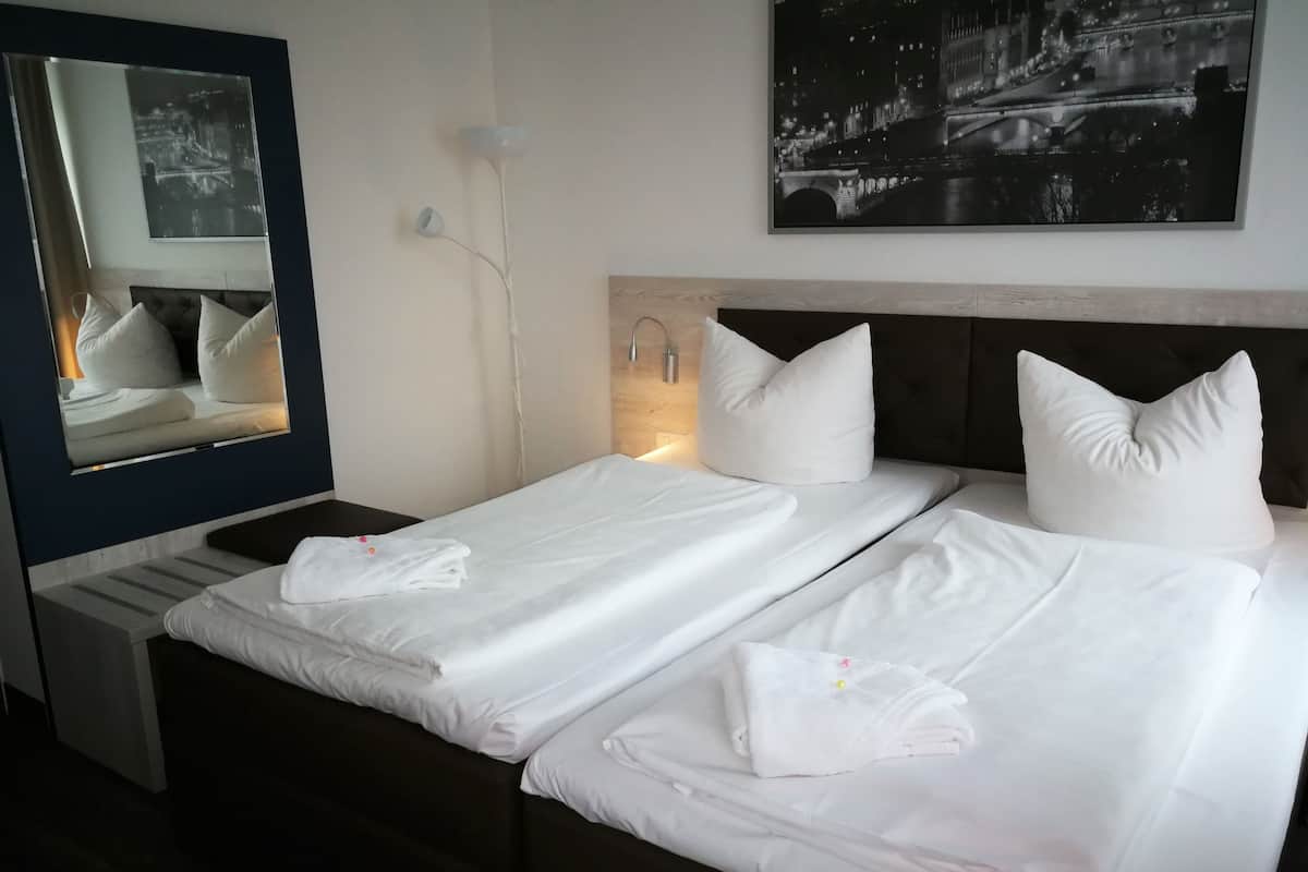 A hotel room with two beds, each with white linens and pillows, a large mirror, and a night view of a cityscape.