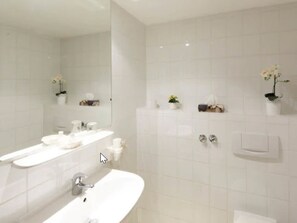 A modern bathroom with white tiles, a large mirror, a sink, and two towel racks. - Hotel NearBy (Laatzen)