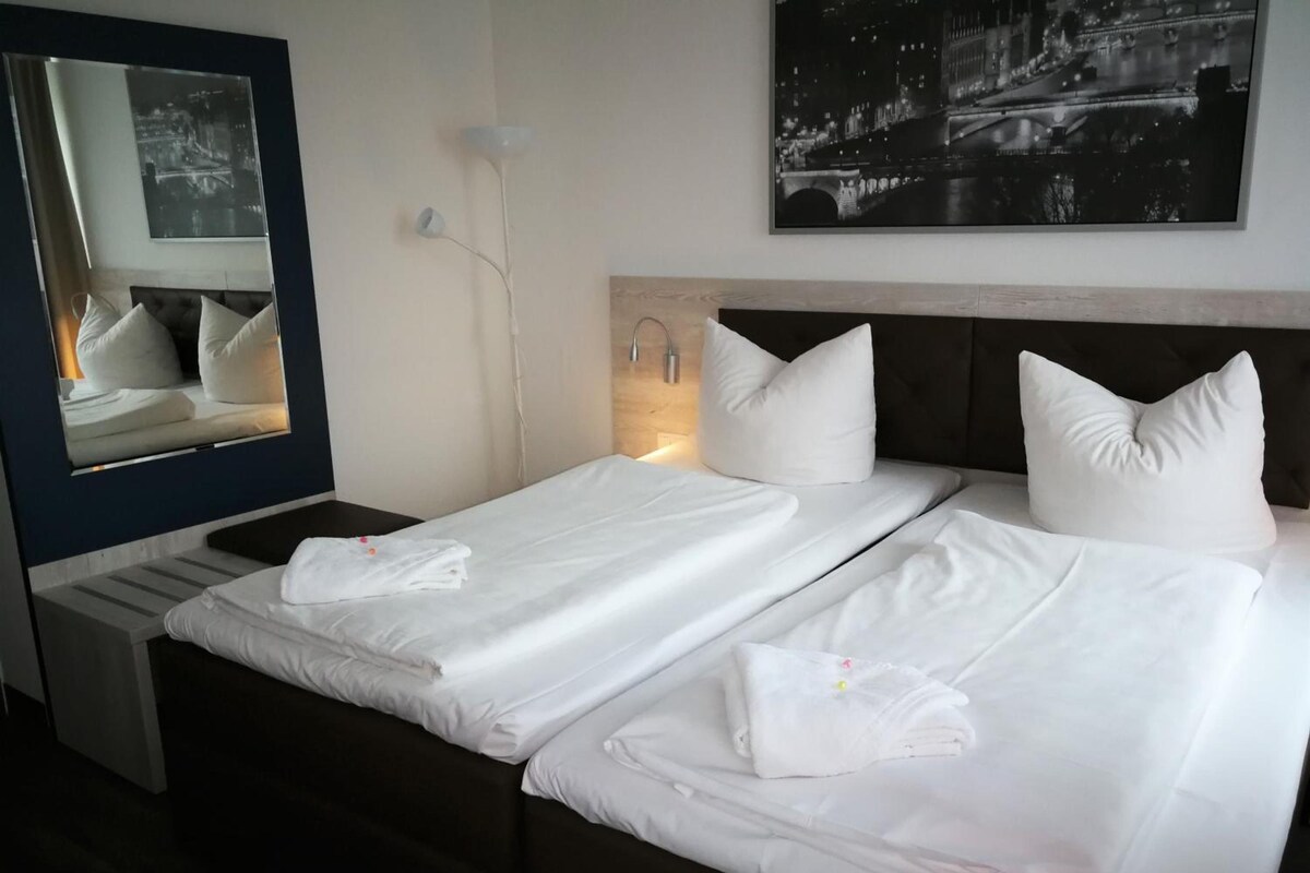 A hotel room with two beds, a large mirror, and a night view poster on the wall.