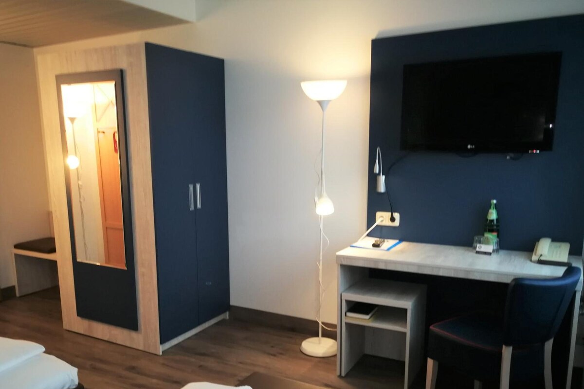 A hotel room with a bed, a desk, a chair, a TV, and a lamp.