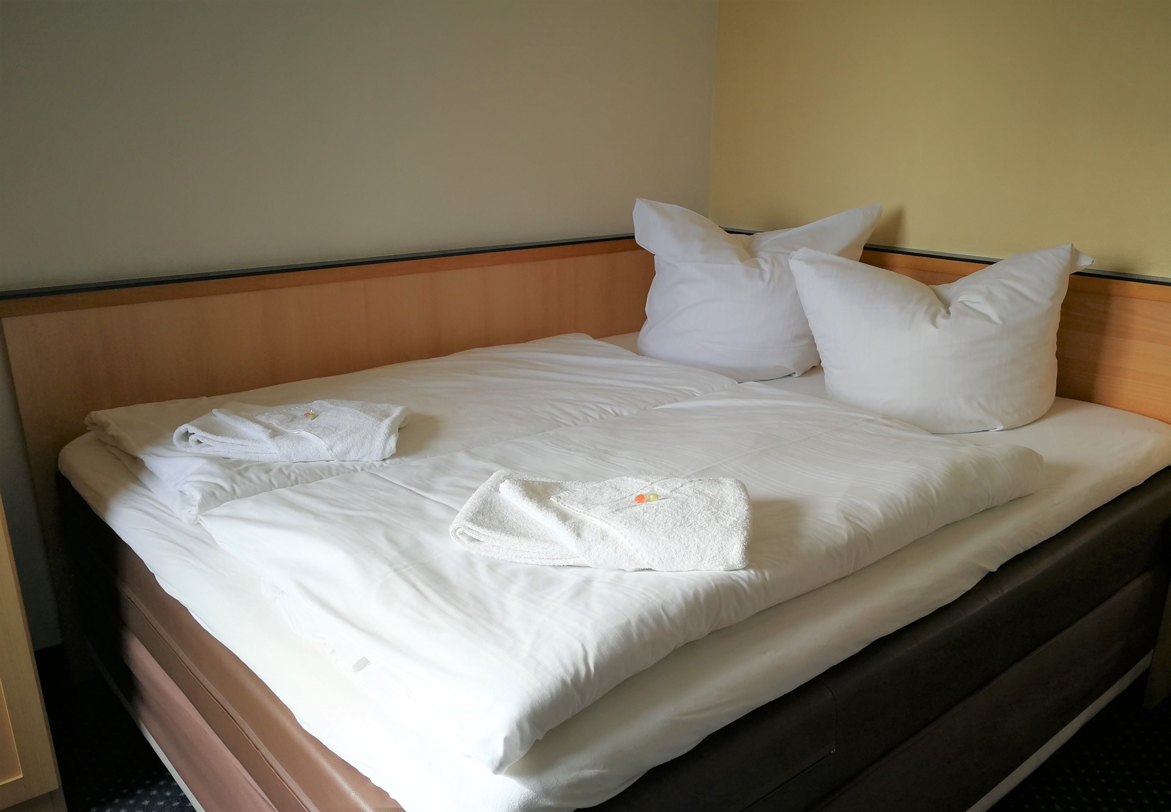 Una cama bien hecha con sábanas y almohadas blancas, un cabecero de madera y una toalla doblada al lado.