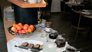 A buffet table with various food items and condiments, including a bowl of fruit, jars of spreads, and a pitcher of iced tea. - Hotel NearBy (Laatzen)