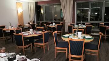 A dining area with multiple tables and chairs, each set with plates, cutlery, and condiments.