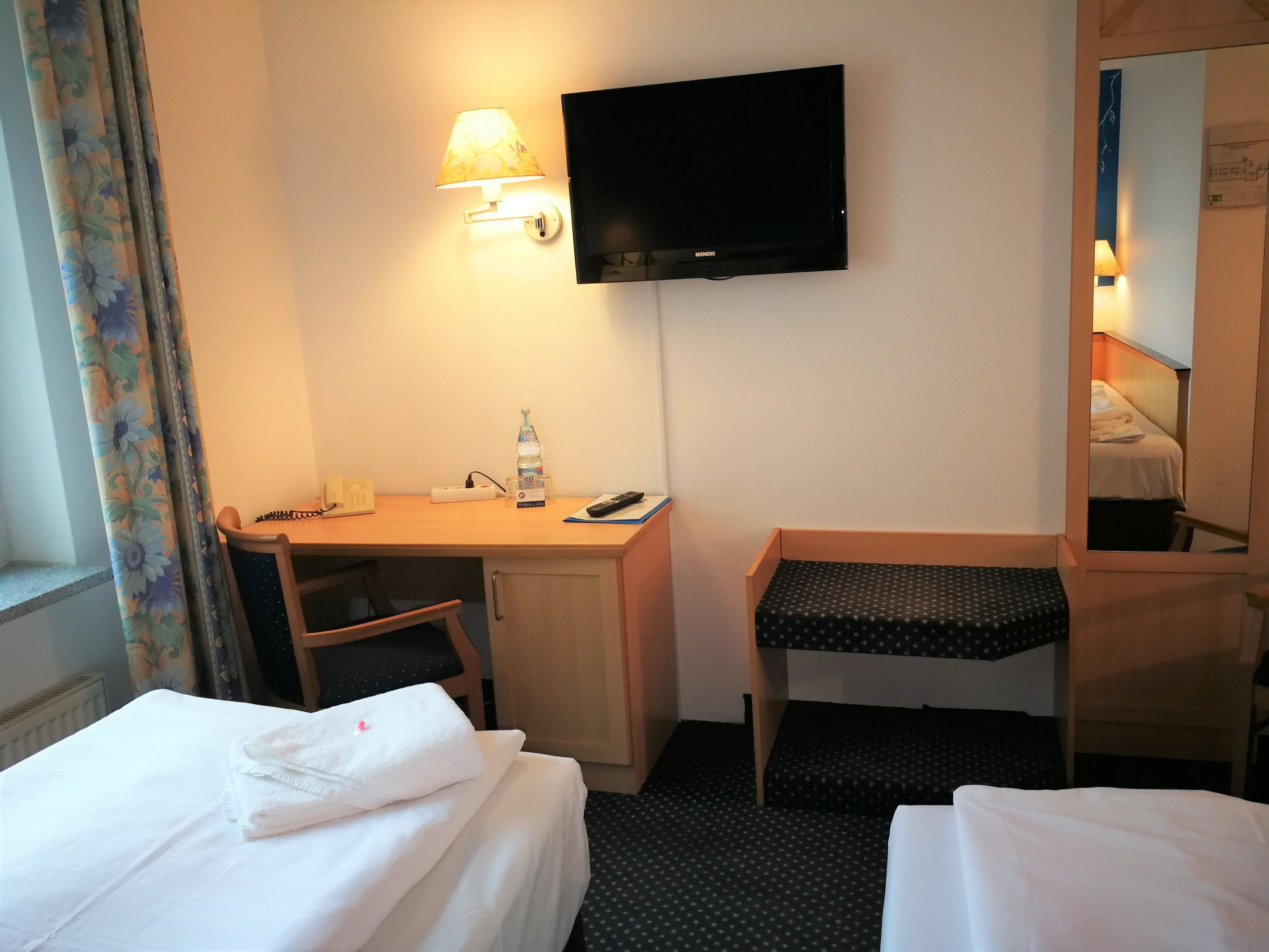 Habitación de hotel con dos camas, un escritorio con silla, televisor y espejo.