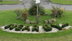 A landscaped area with trimmed bushes, a central rock feature, and a crosswalk. - Hotel NearBy (Laatzen)
