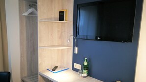 A hotel room with a desk, a telephone, a bottle of water, a remote control, and a television mounted on the wall. - Hotel NearBy (Laatzen)