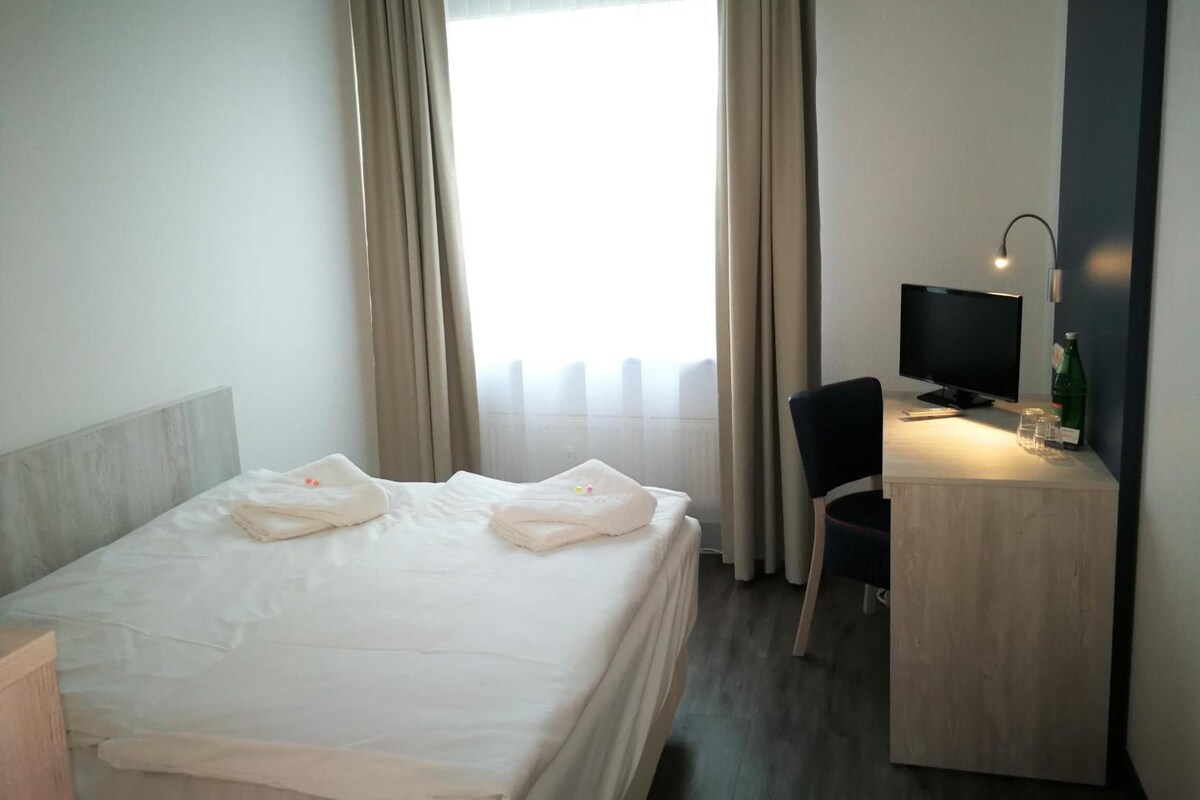 A hotel room with a bed, a desk with a computer, and a chair.