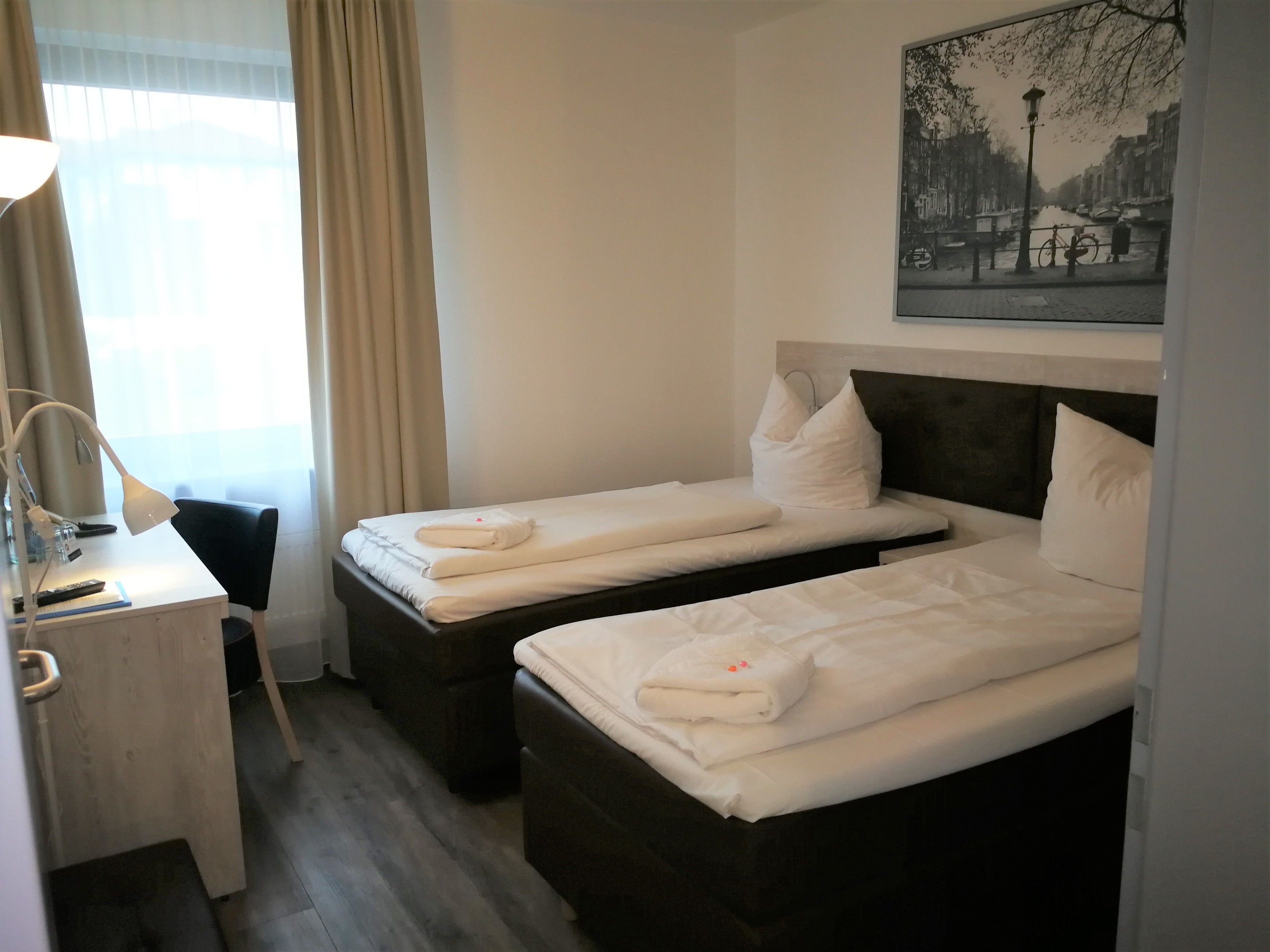 Ein Hotelzimmer mit zwei Betten, einem Schreibtisch mit Lampe und einem Bild an der Wand.