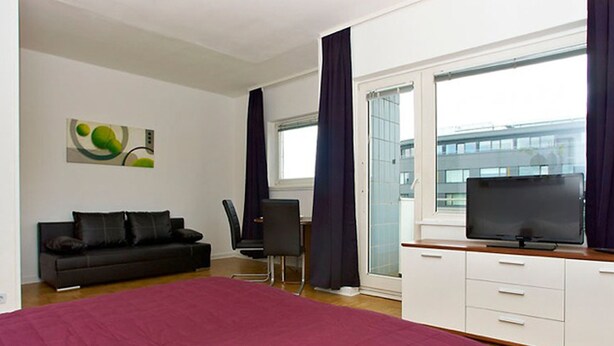 A modern bedroom with a large bed, a black sofa, a desk, and a TV.