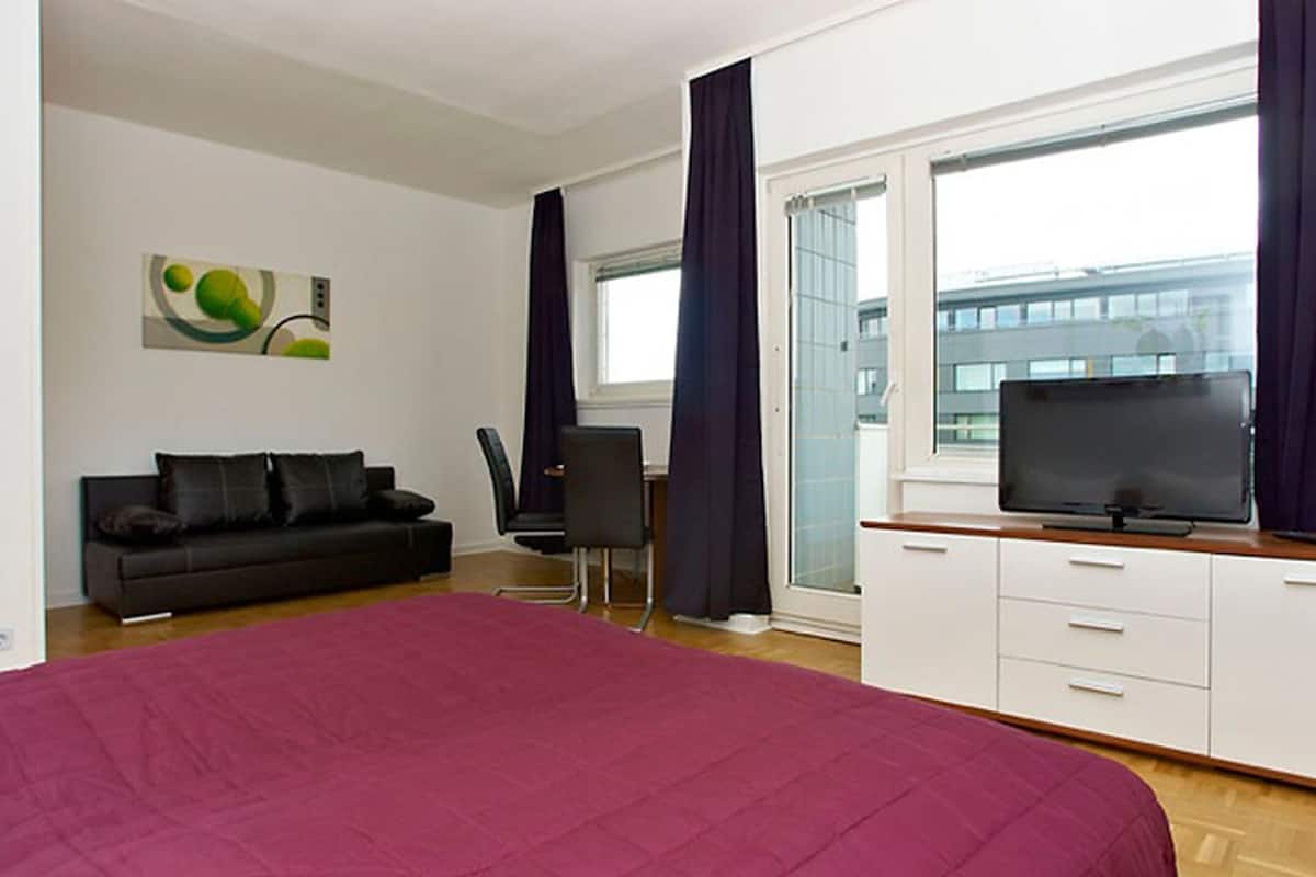 A modern bedroom with a large bed, a black sofa, a desk, and a TV.