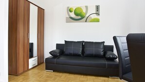A modern living room with a dark leather sofa, a wooden wardrobe, and a contemporary abstract painting on the wall.
