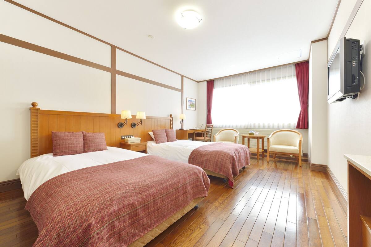 Una habitación de hotel con dos camas, un escritorio, una silla y un televisor.
