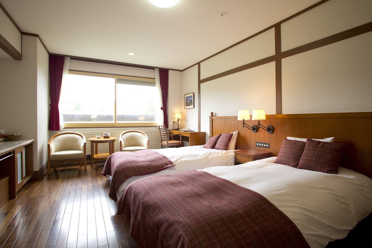 Una habitación de hotel con dos camas, un escritorio, una silla y una ventana con cortinas.