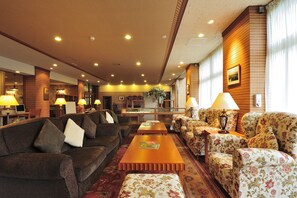 Un hall d’hôtel avec un canapé marron, des fauteuils à motifs floraux, une table basse en bois et un comptoir de réception.