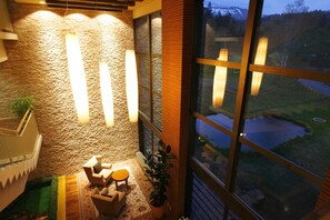 A cozy seating area with a stone wall and large windows overlooking a pond. - Asahidake Onsen Hotel Deer Valley (Higashikawa)