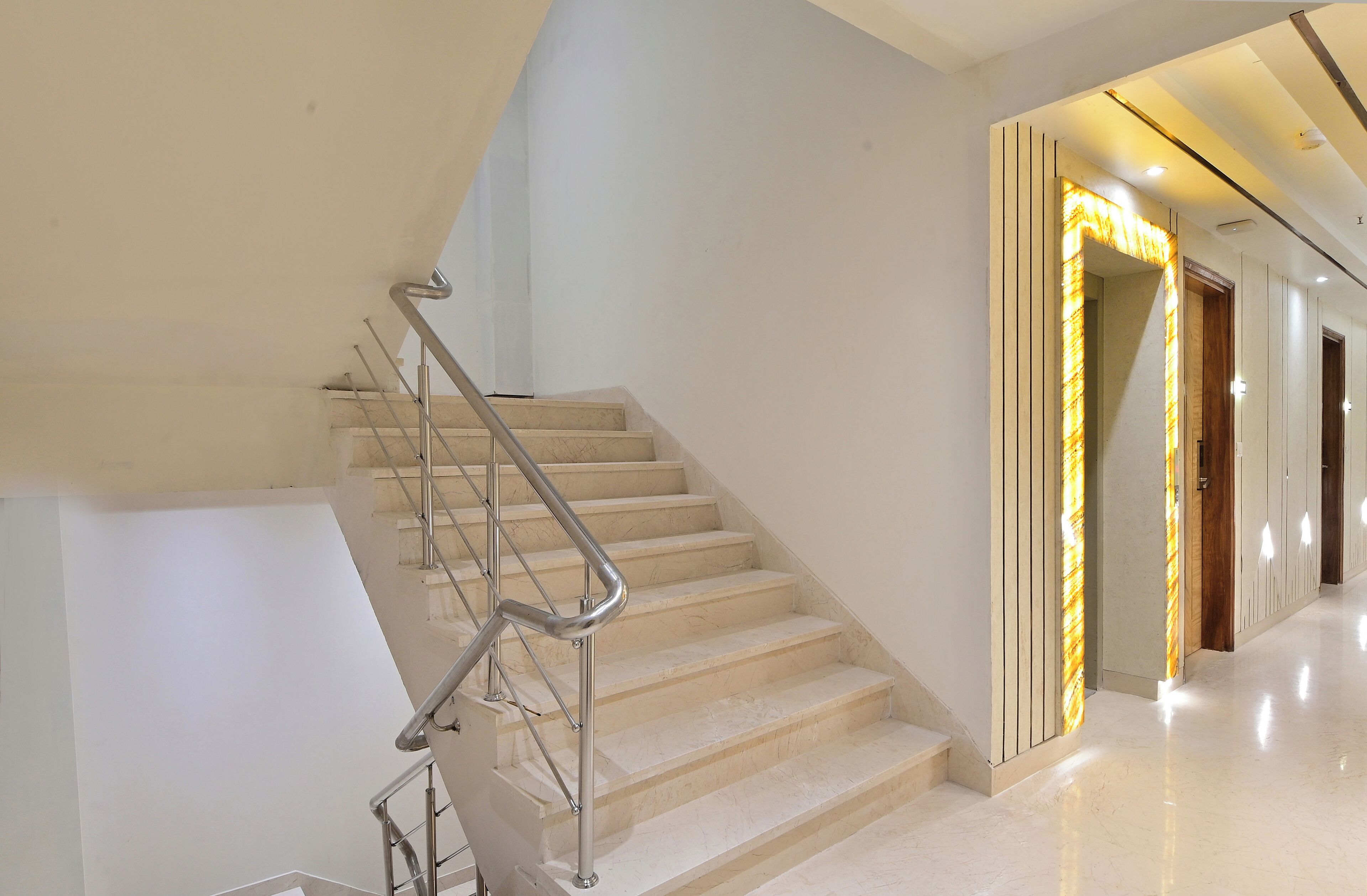 A modern staircase with a metal handrail, leading to a hallway with a bright, illuminated archway.