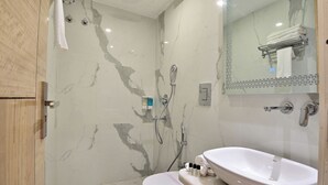 A modern bathroom with a marble shower wall, a white sink, and a glass-enclosed shower. - Hotel Aman International at New Delhi Station (New Delhi)