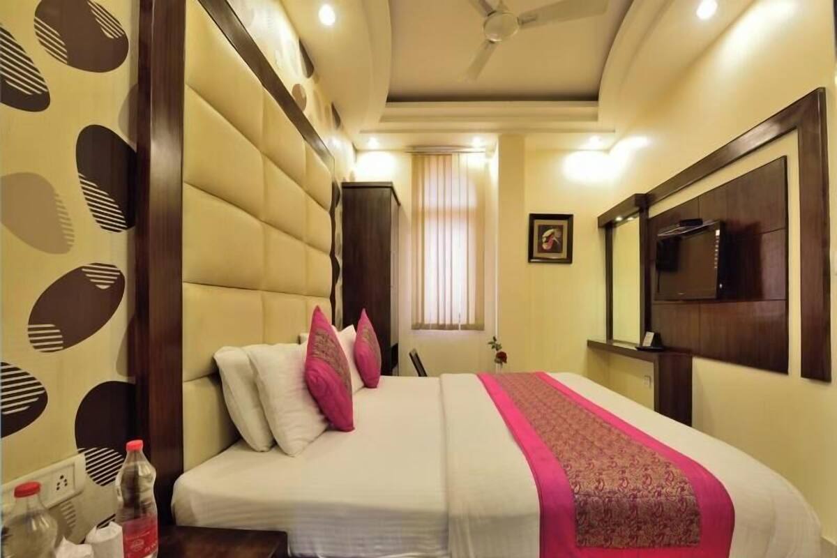 Habitación de hotel con cama, televisión, ventilador de techo y ventana con cortinas.