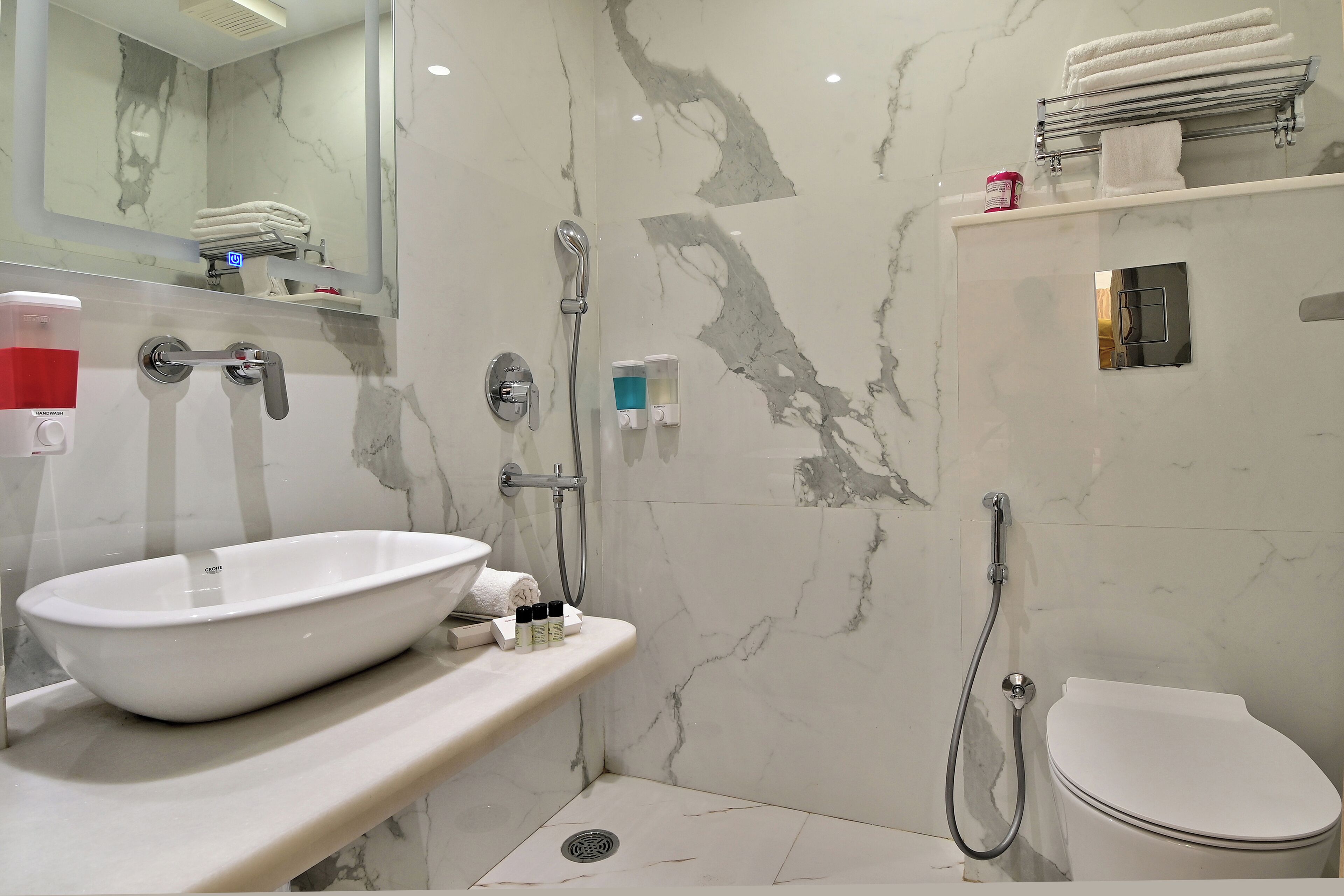A modern bathroom with a white sink, a handheld showerhead, a toilet, and a mirror.