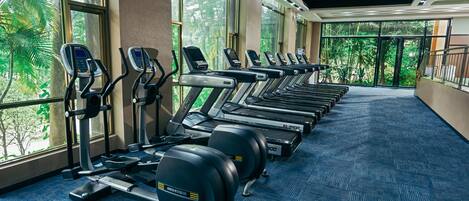 Un gimnasio con cintas de correr, elípticas y máquinas de pesas dispuestas en filas.