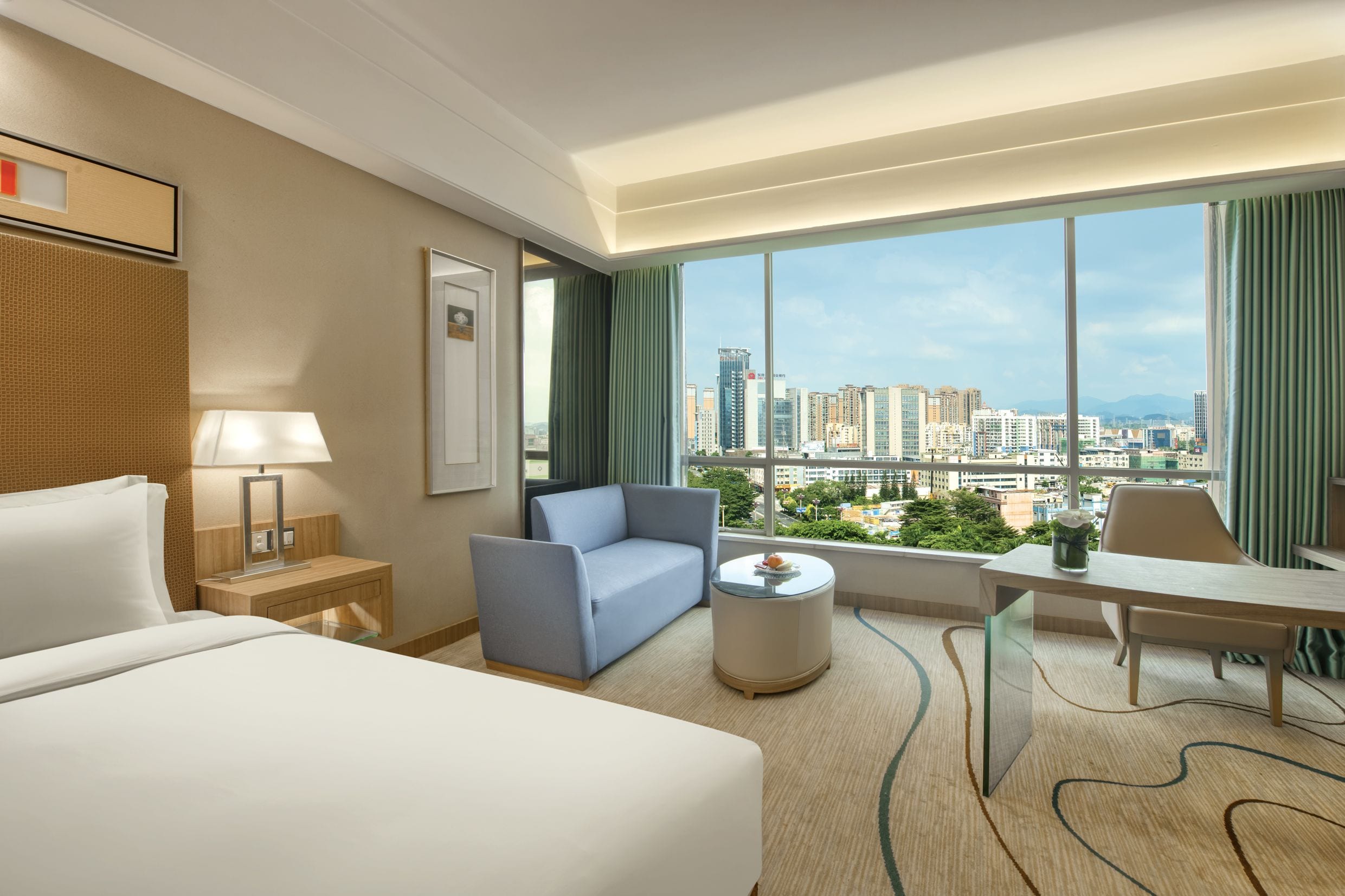 Habitación de hotel con cama, sofá, escritorio y vistas a la ciudad.