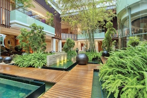 A modern indoor atrium with a central water feature, wooden flooring, and lush greenery.