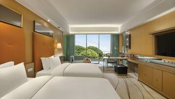 A hotel room with two beds, a desk, a chair, a TV, and a large window with a view of trees.