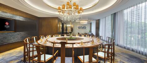 A conference room with a round table, chairs, a chandelier, and a television on the wall.