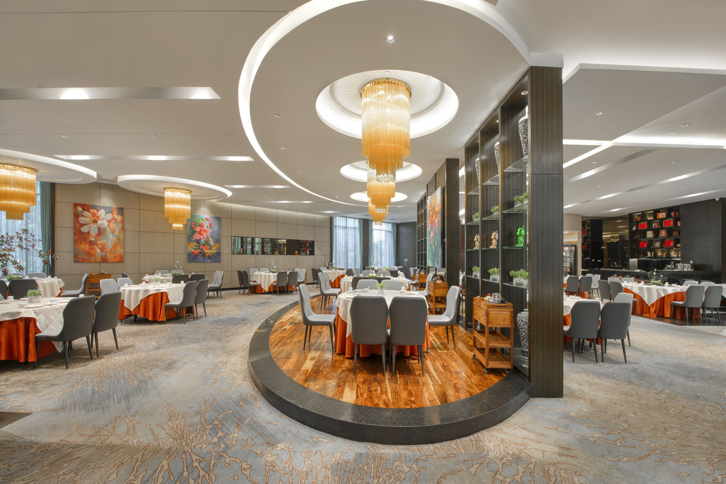 A spacious dining area with round tables, chairs, and a central chandelier.