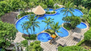 Un resort con varias piscinas, palmeras y una zona de estar techada.
