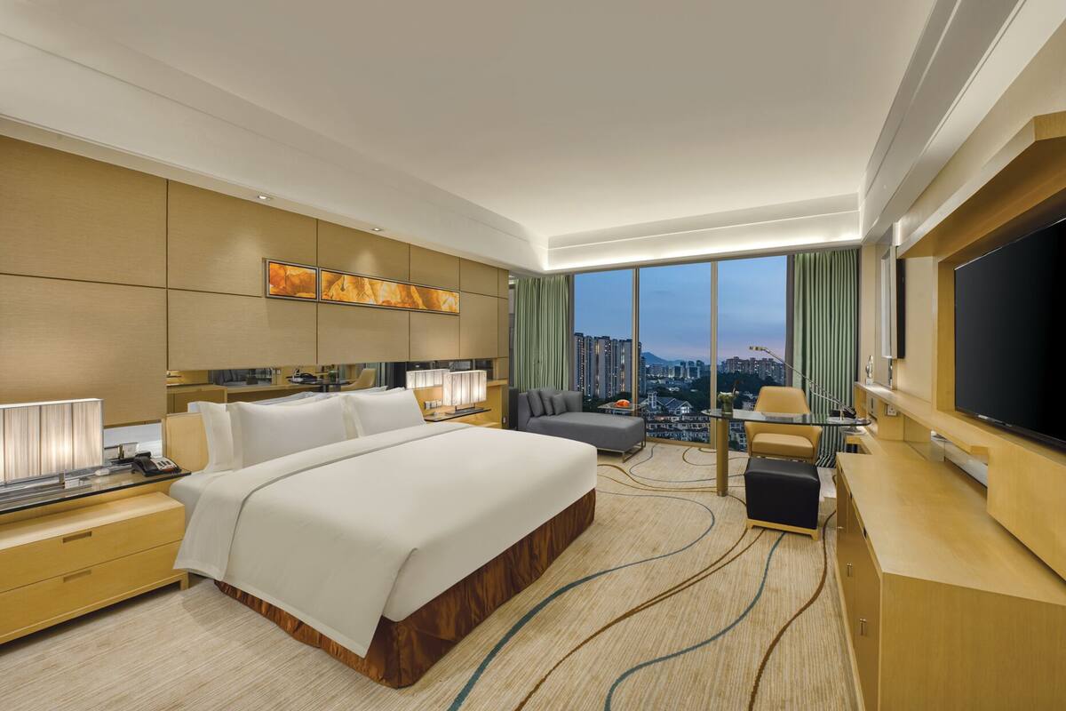 Habitación de hotel moderna con una cama grande, un escritorio, un televisor y vistas a la ciudad.