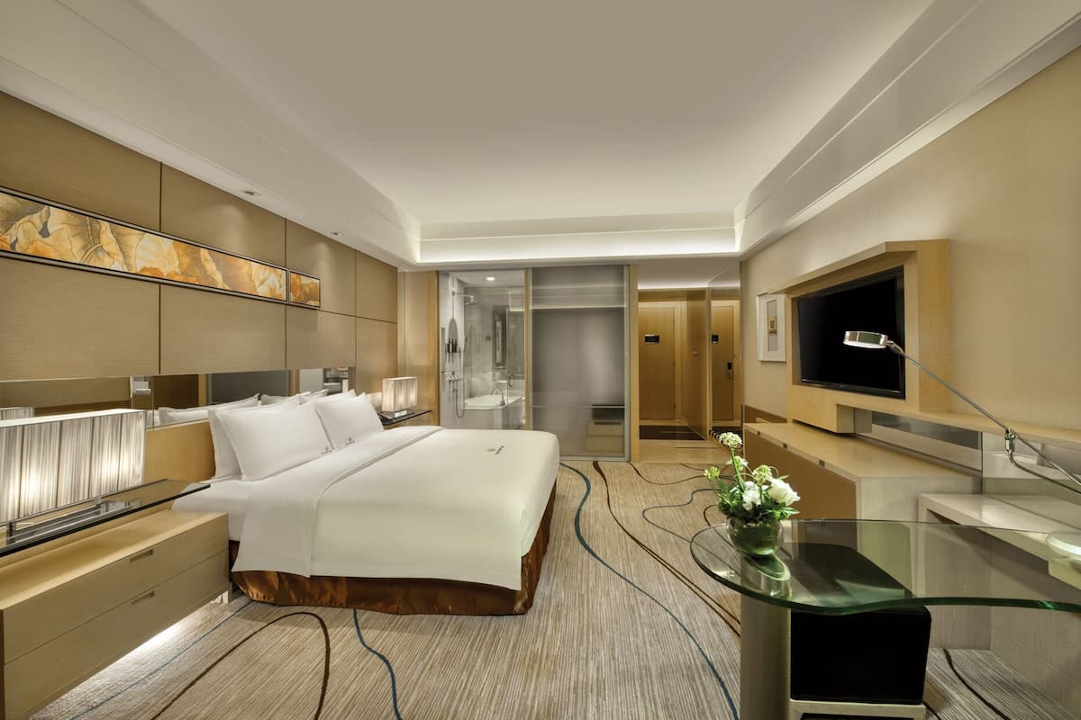 Una habitación de hotel moderna con una cama grande, una mesa de centro de vidrio, un televisor y un vestidor.