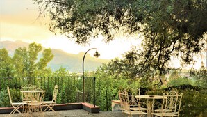 An outdoor patio with metal chairs and tables, surrounded by greenery and a view of distant mountains. - Antico Borgo Etneo Country Hotel (Calatabiano)