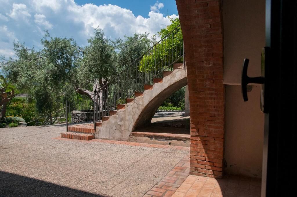 A stone staircase leading to a building entrance, surrounded by greenery and a clear sky.