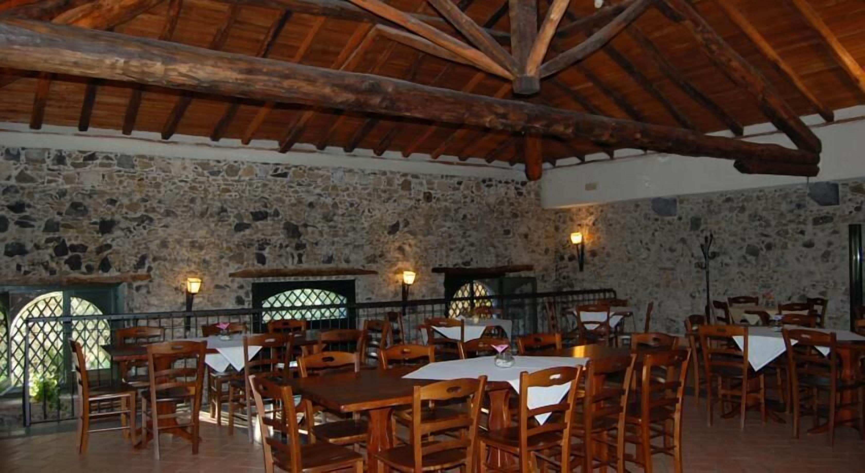 A rustic dining area with stone walls, wooden tables, and chairs.