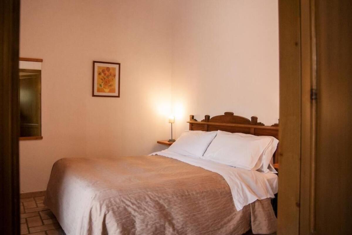 A neatly made bed with a wooden headboard, a bedside lamp, and a framed picture on the wall.