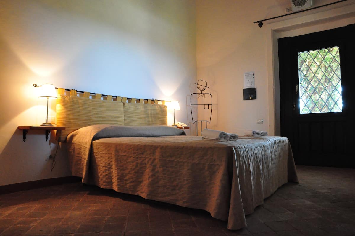 A bedroom with a bed, bedside lamps, a wall clock, and a window with a view.