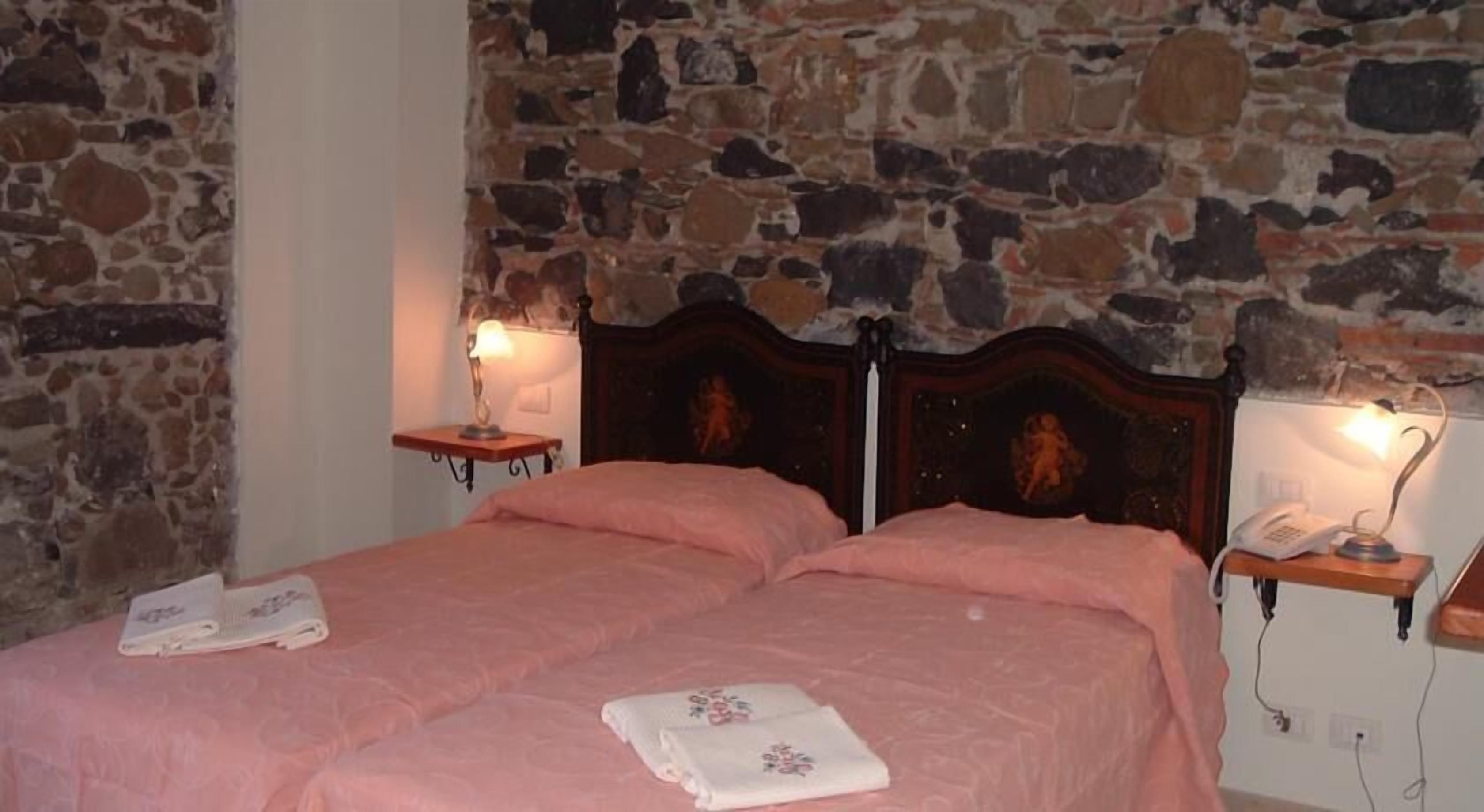 A double bed with pink bedding, two bedside tables with lamps, and a stone wall.