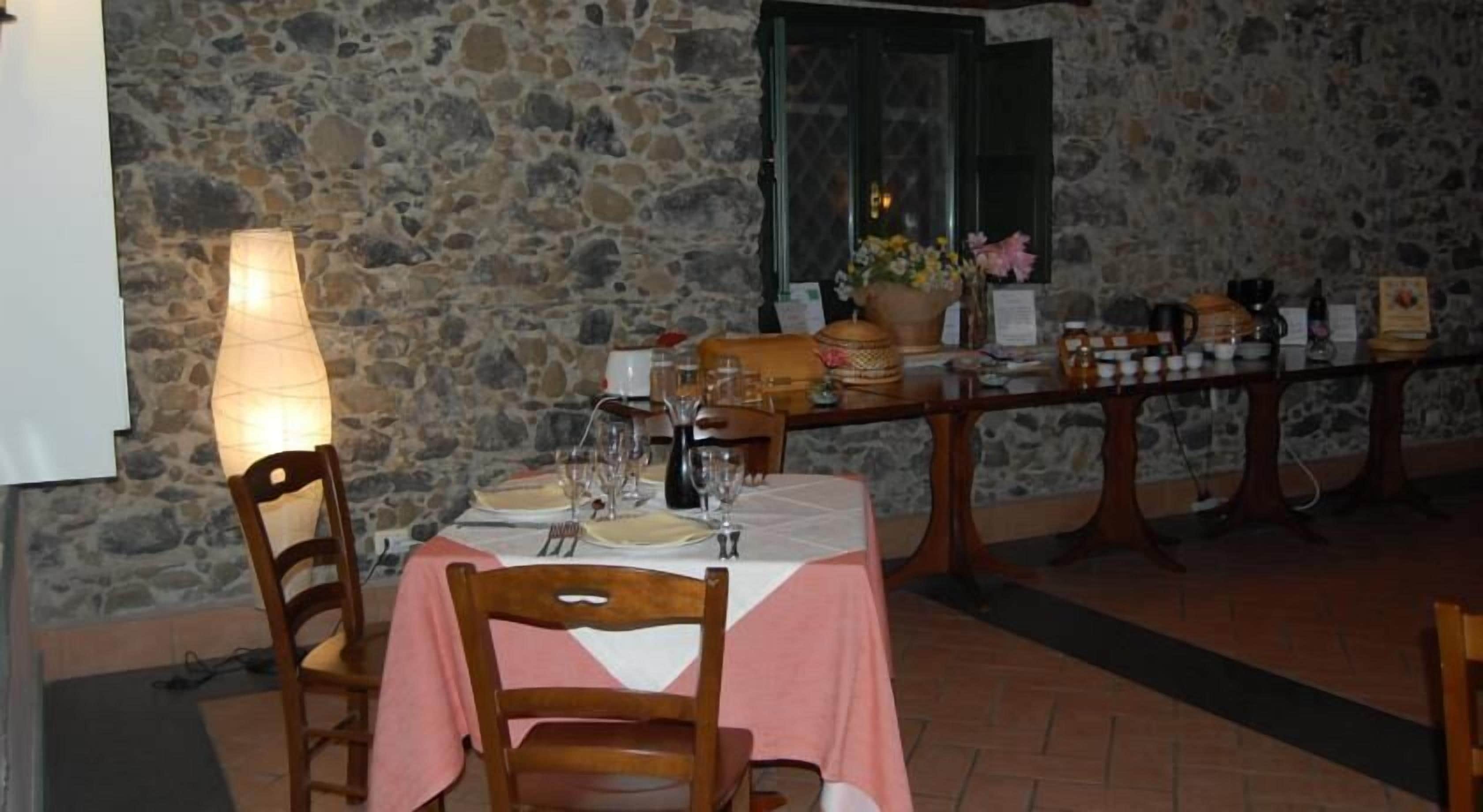 Mesa lista para comer con sillas, pared de piedra y una ventana al fondo.