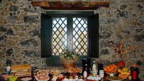 A stone-walled room with a table set for a meal, a window with lattice, and a vase with flowers. - Antico Borgo Etneo Country Hotel (Calatabiano)
