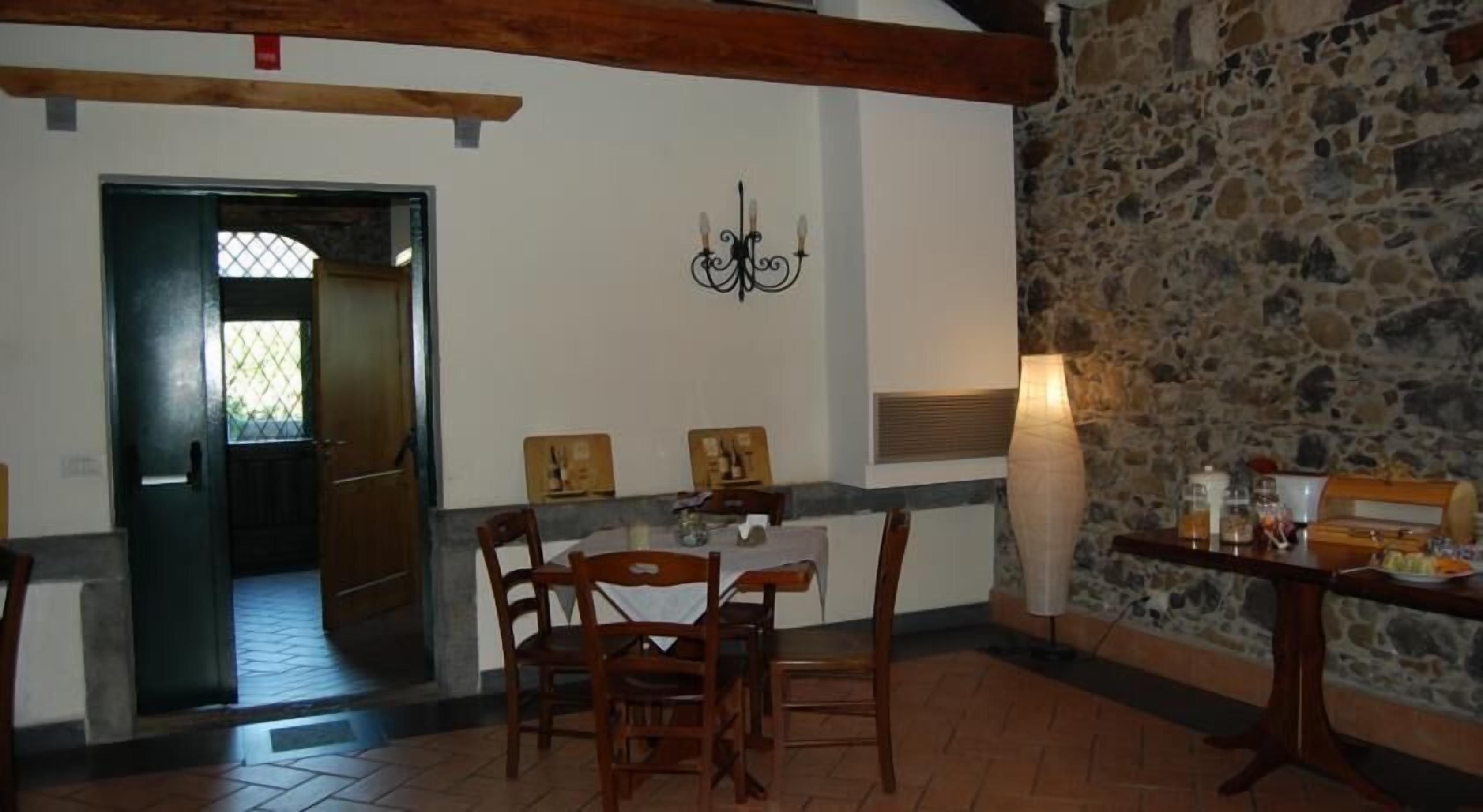 A dining area with a stone wall, wooden chairs, a table with a vase, and a chandelier.